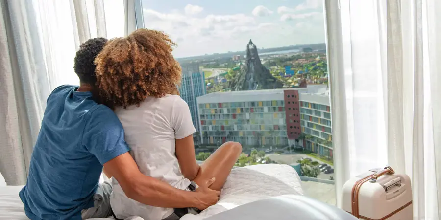 A couple sits on a bed and looks at a water park outside their hotel room window